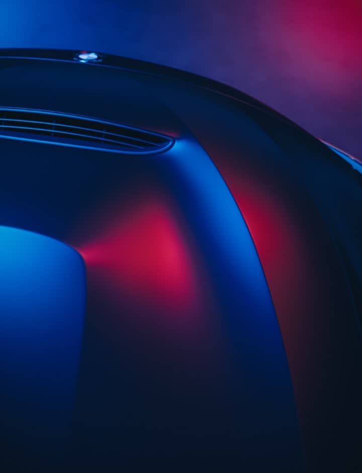 Close-up of a sleek, curved car surface reflecting blue and red lights, with a vent near the top left—its futuristic aesthetic subtly hinting at used gas turbine technology now rendered obsolete.