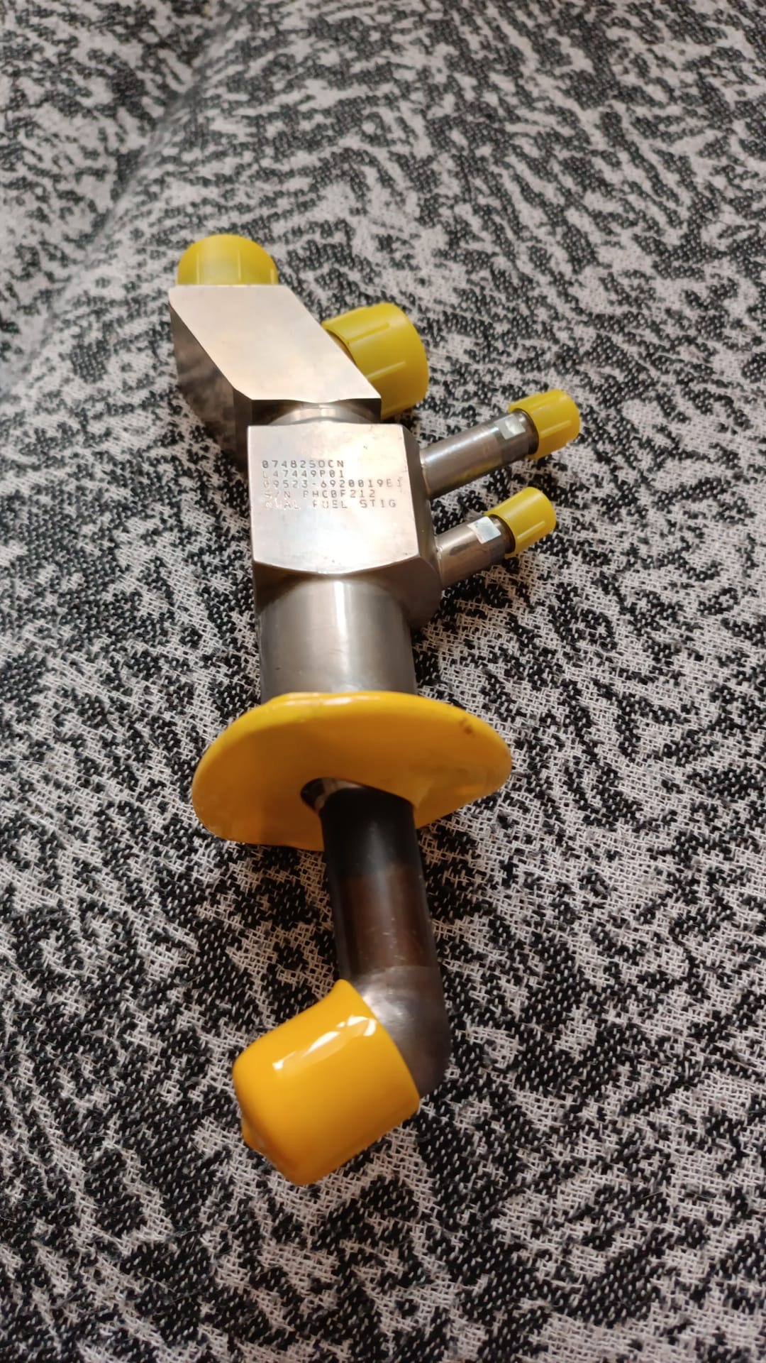 Four overhauled OH Dual Fuel DF Nozzles (L47449P01) with metallic finishes—each featuring three tubes capped in yellow and a yellow flange—rest on a patterned gray and white surface, highlighting their essential role as LM2500 spare parts for heavy industry applications.