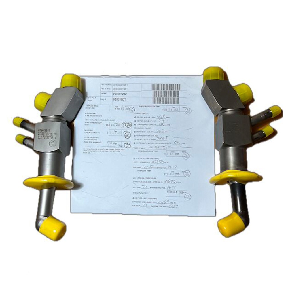 Two overhauled OH Dual Fuel DF Nozzles (L47449P01), each featuring yellow caps, are positioned on either side of a document containing printed text and handwritten notes, all set against a white background.