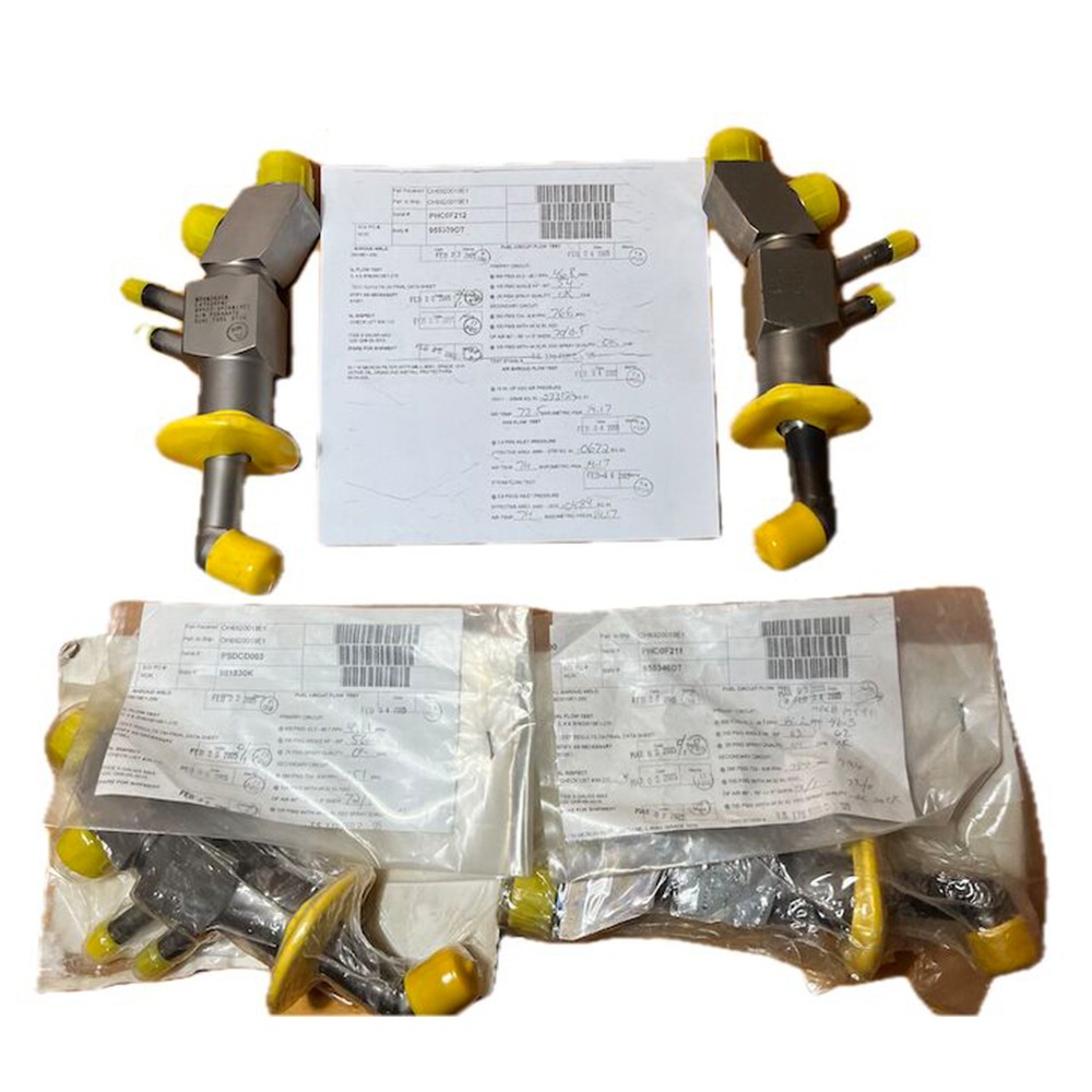 Four overhauled OH Dual Fuel DF Nozzles L47449P01, featuring yellow caps and commonly used in gasturbine applications such as the LM6000, are displayed—two placed above two more identical nozzles inside clear plastic bags. Three paper documents with printed text and barcodes are visible above the nozzles.