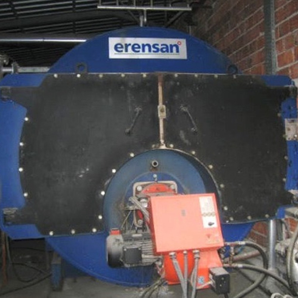A 1 Set of Auxiliary Steam Boiler 5 t/h for a MAN HFO Power Plant, industrial and blue with a flat black front panel and red control unit below, is surrounded by pipes and set against a brick wall.