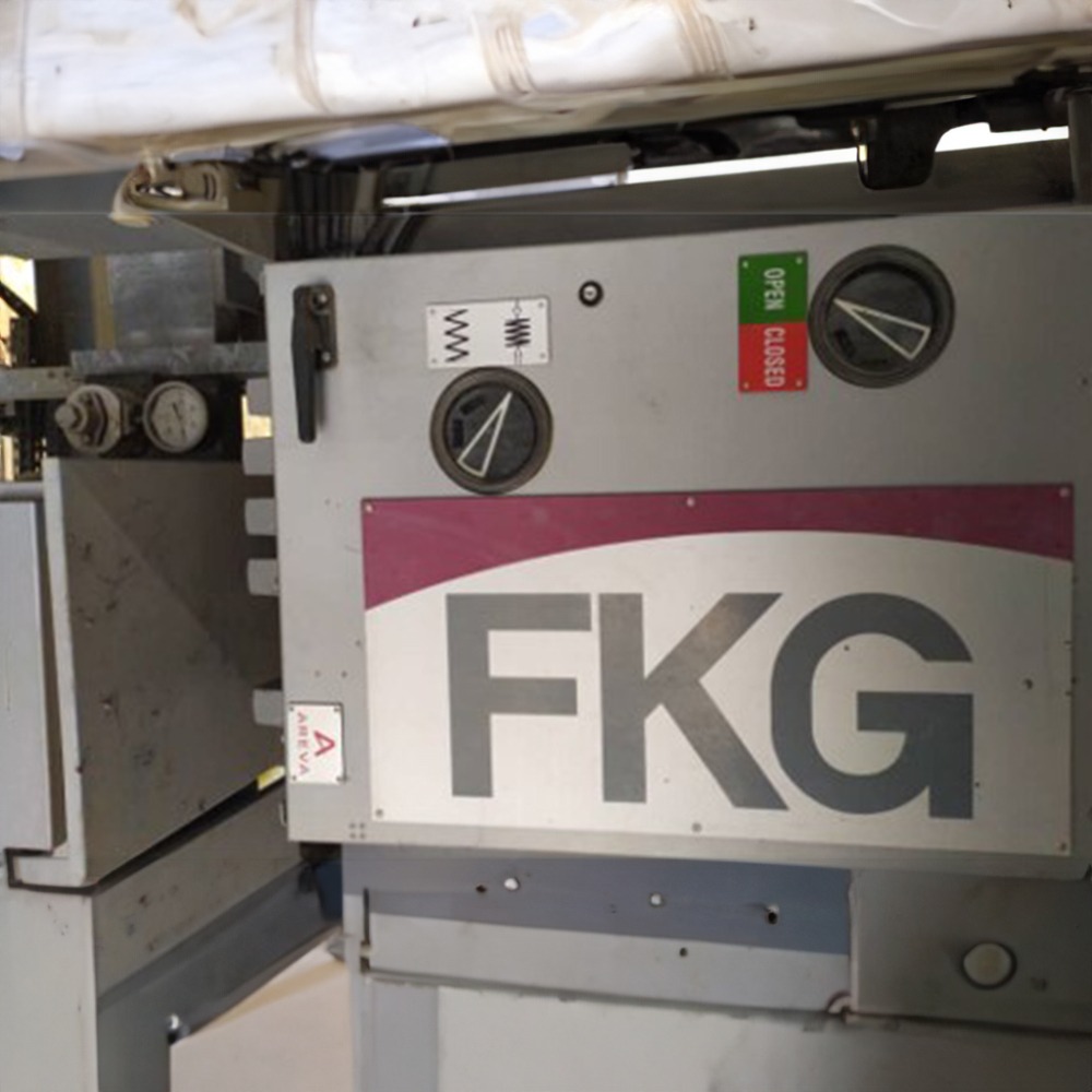 A close-up of industrial equipment featuring a metal panel with dials, gauges, and clearly labeled buttons, displaying the letters FKG. A fabric or sheet is partially visible at the top of the machine, indicating that this may be part of a GE Counter for FKG2M Circuit Breaker setup.
