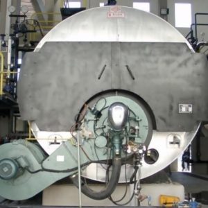 Two new 12 t/h steam boilers, featuring metal piping, gauges, and control panels, are installed in a factory. Each boiler has a round silver front with a central burner assembly connected to various hoses and machinery.