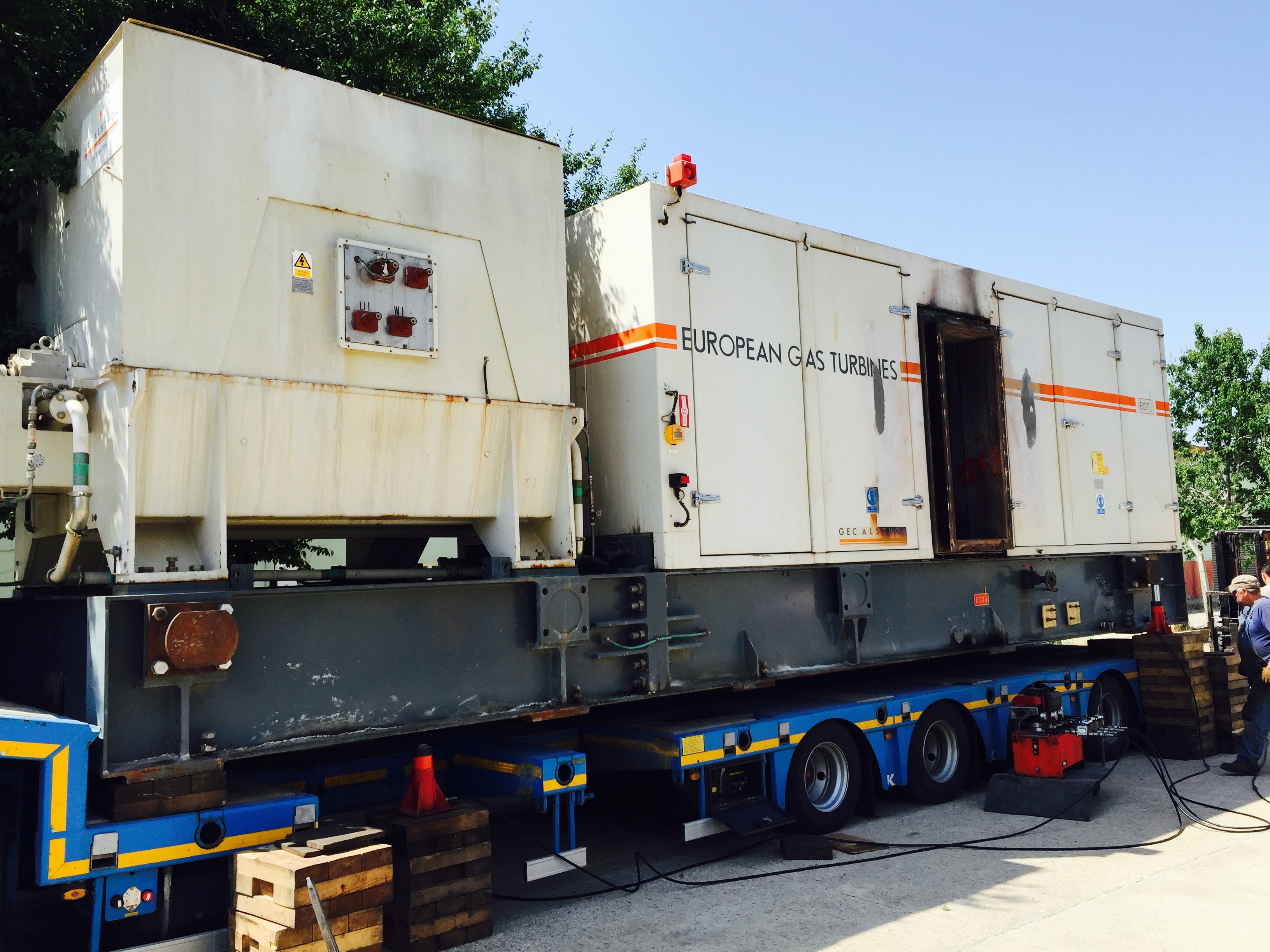Large industrial equipment labeled Siemens SGT 200 Gas Turbine Packages is mounted on a trailer, surrounded by wooden blocks and traffic cones, with trees and sky visible in the background. This impressive example of heavy industry showcases components from the SGT 200 series, highlighting its role as a critical spare part in advanced energy applications.