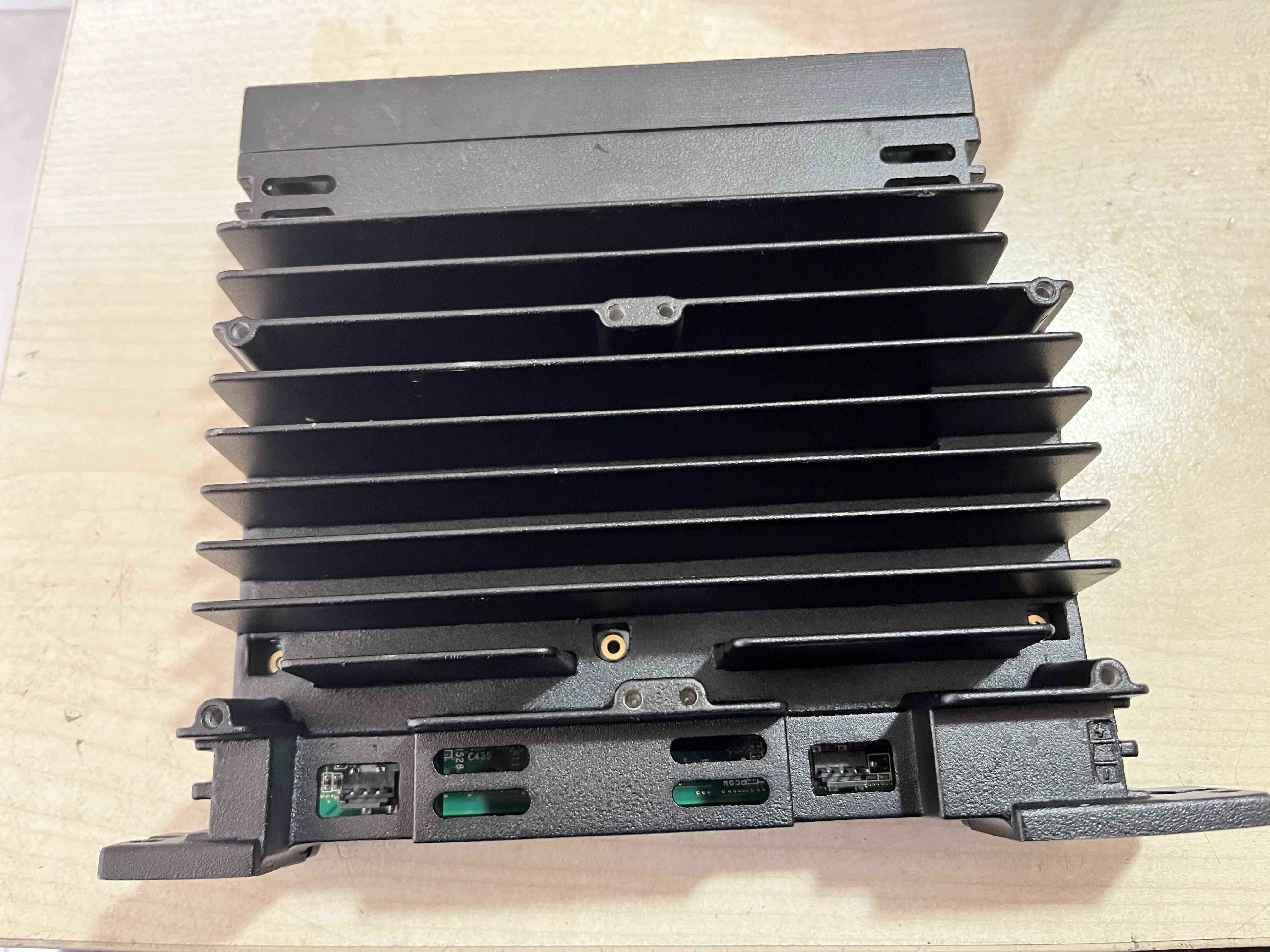 A refurbished black metal heat sink with horizontal fins is mounted on a light wooden surface, with several green circuit board components from a used GE Energy IS420UCSBH4A UCSB controller module visible at the bottom.
