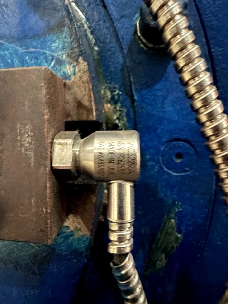 A close-up of the Wanted cable 362A1053P031, designed for the GE gas turbine flame sensor, connected to a flexible conduit on a blue industrial machine. The cable fitting shows engraved serial numbers and specifications.