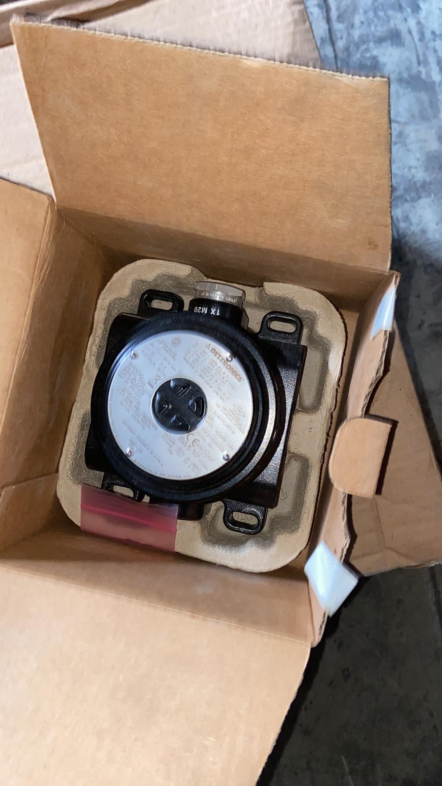 A Det-tronics STB1A2MW Model STB Sensor Termination Boxes Separation Kit, featuring a black exterior with a white label, is securely packed in a cardboard box with molded padding and positioned on a concrete floor.