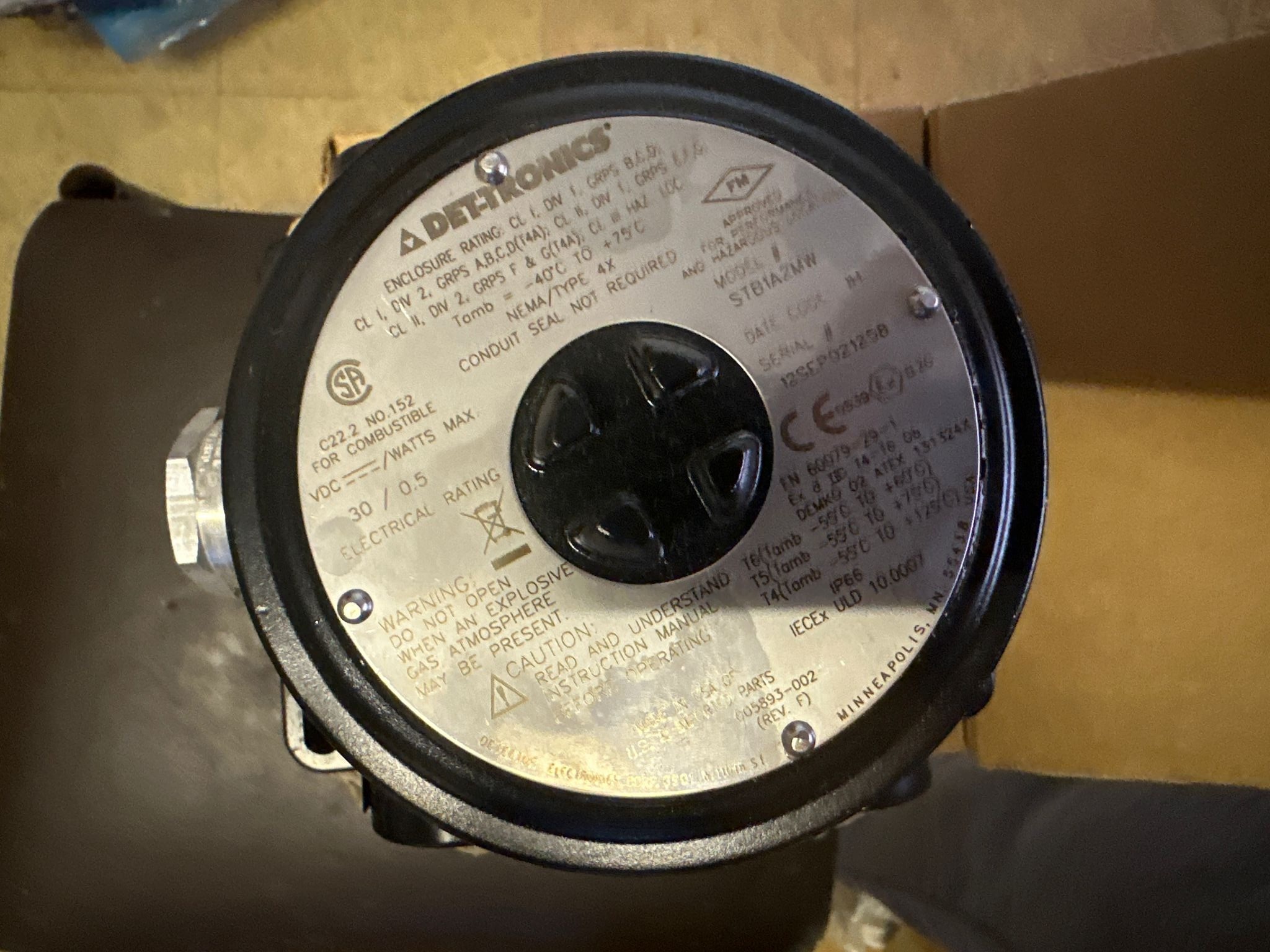 Close-up of a Det-tronics STB1A2MW Model STB Sensor Termination Boxes Separation Kits label with technical specifications, warnings, certification logos, and electrical ratings engraved on a metal circular plate, mounted on dark heavy industry equipment such as an LM2500 gas turbine.