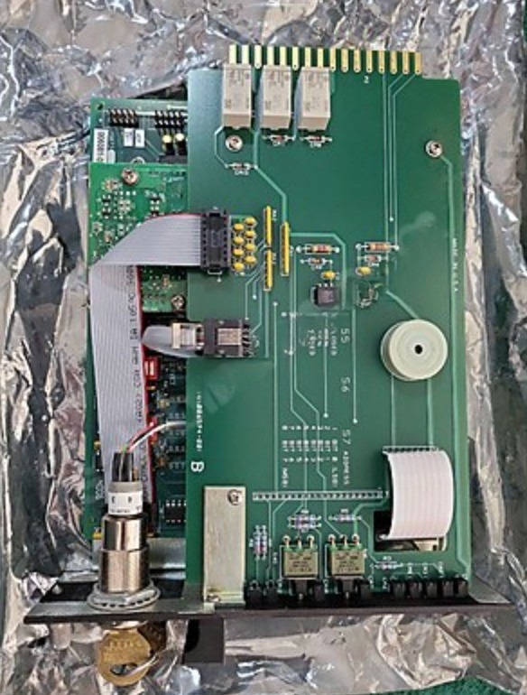 A Det-tronics EAGLE QUANTUM LOCAL CONTROL UNIT EQ2100LC Logic Controller—with connectors, ribbon cable, and pins—ideal as a spare part, rests on crumpled metallic foil.