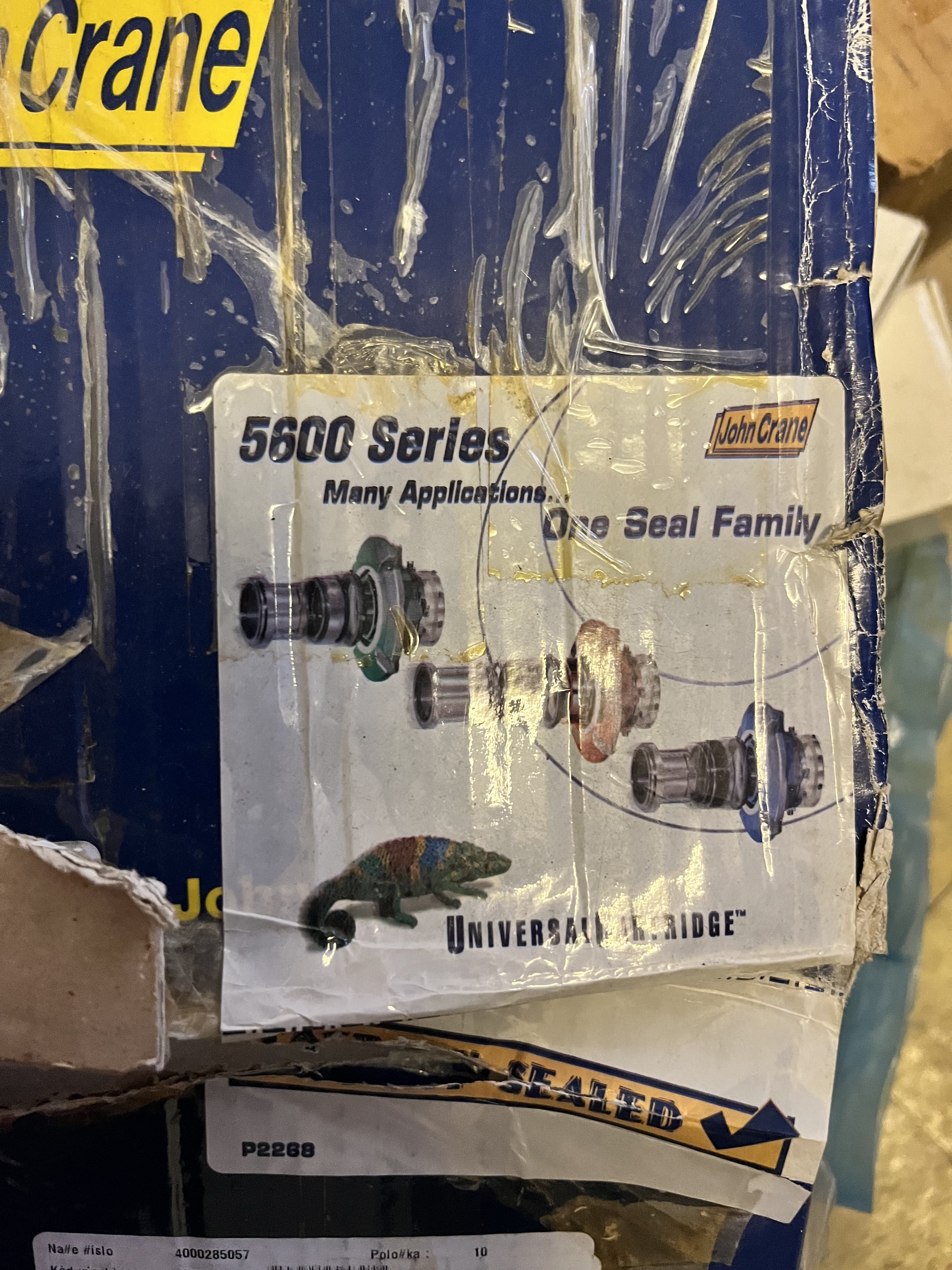 A close-up of a damaged box with a label showing a mechanical diagram for the John Crane 5600 Series universal cartridge, featuring images of shaft seals used in gas turbine and LM6000 applications, plus the text “Many Applications. One Seal Family.”.