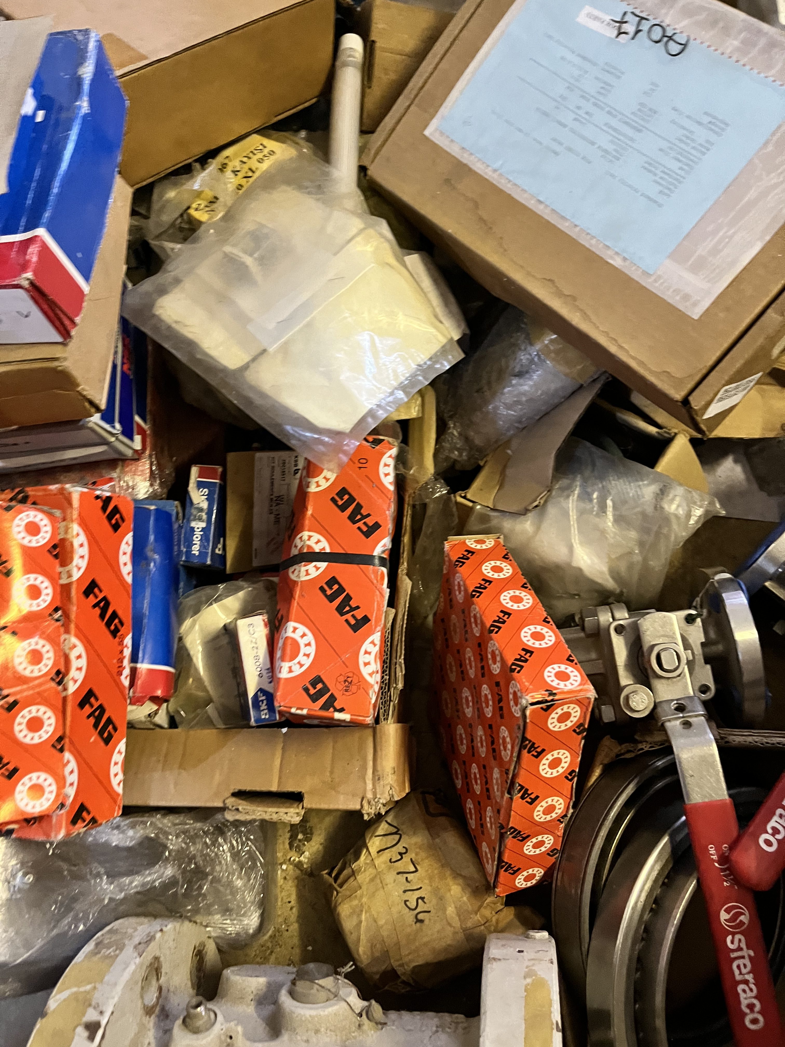 A cluttered assortment of used mechanical parts and boxes, including FAG-branded packaging, LM6000 components, and documents, all piled together in a disorganized manner.