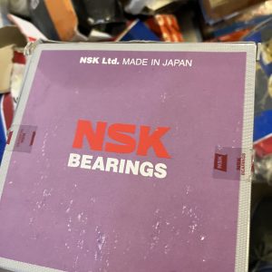 A person holds a used purple box labeled NSK BEARINGS with NSK Ltd. MADE IN JAPAN at the top. The worn box, likely containing LM6000 spare parts, is surrounded by other boxes in the background.