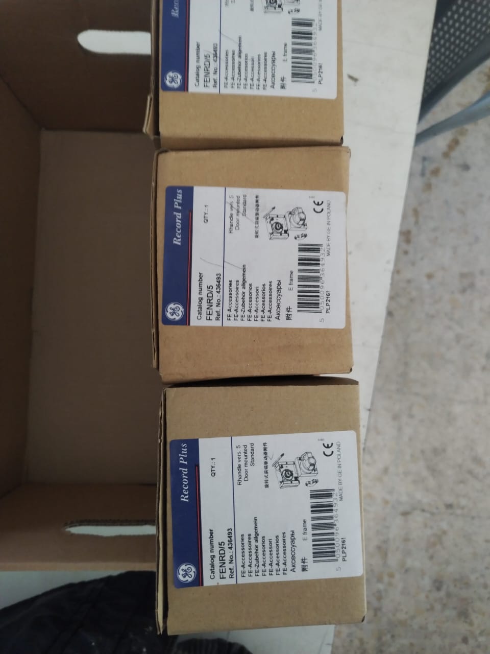 Three brown boxes labeled Sold 3 pcs OBSOLETE GE FENRD/5 Door Mounted Extended Rotary Handle for GE Circuit Breaker with technical details and barcodes are stacked in a cardboard container on a light-colored surface.