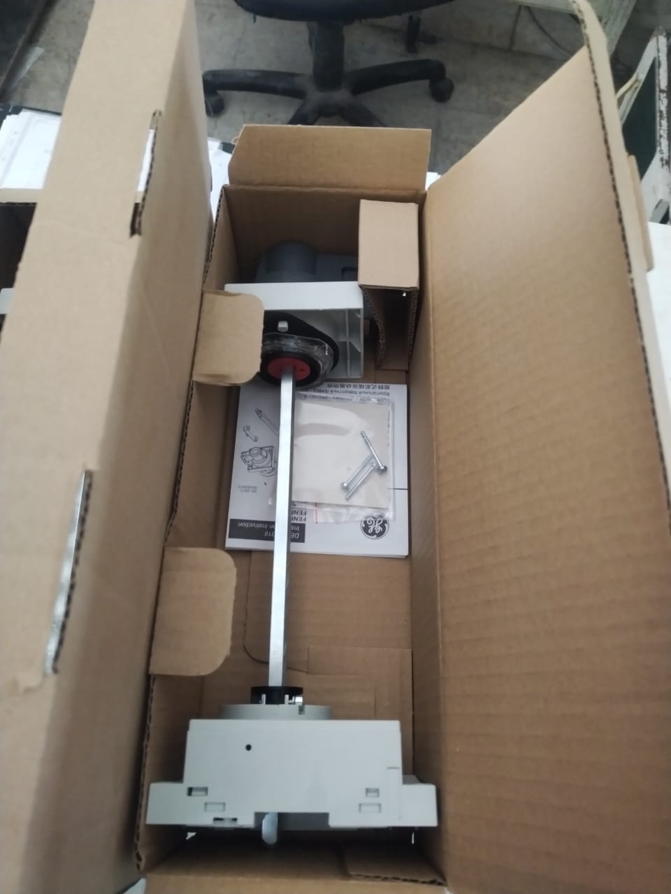 A cardboard box contains 3 used obsolete GE FENRD/5 door mounted extended rotary handles for GE circuit breakers, complete with instruction manual and small spare parts. An office chair appears in the background.