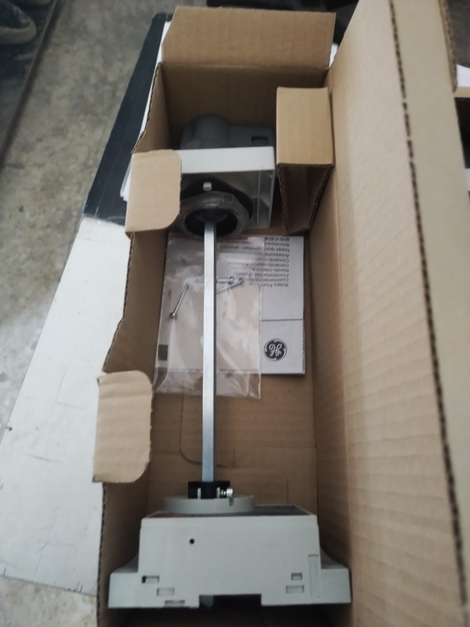 Three OBSOLETE GE FENRD/5 Door Mounted Extended Rotary Handles for GE Circuit Breakers, gray with long metal rods and partially assembled, are packed in an open cardboard box with packaging material and instructions.