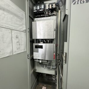 An open AVAILABLE MARK IV AND MARK V CONTROLS 01 industrial electrical cabinet shows circuit breakers, wiring, metal enclosures, technical diagrams on the door, and batteries at the bottom; the setup looks organized and well maintained.