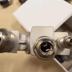 Close-up of a full set of fuel nozzles L31809P12 FOR LM2500, showing two different nozzle sizes resembling turbine attachments, against a blurred background with a white rectangular object.