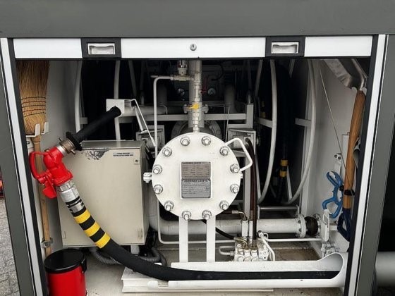 A close-up of industrial machinery inside a compartment displays pipes, valves, gauges, a broom, a bucket, and the red fuel nozzle of the Available Refueller Refueler Tank 10000 m3 connected to a hose among mechanical components.