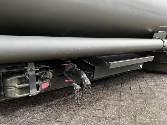 Close-up of the underside of the Available Refueller Refueler Tank 10000 m3, featuring pipes, hoses with metal caps and chains, plus a secured container above a brick-paved surface.