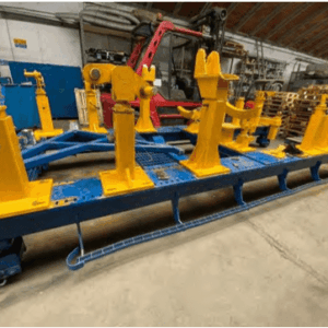 A large blue and yellow metal industrial fixture is positioned inside a spacious warehouse with a concrete floor; shelves and stacked pallets are visible in the background. Stand for gas turbine LM6000 and LM2500