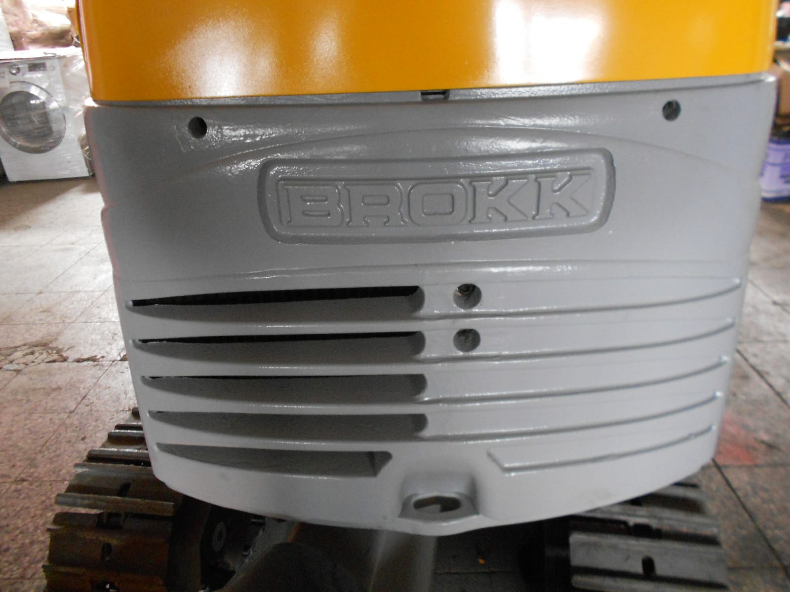 Close-up of the back of a yellow and gray DEMOLISHING UNIT BROKK 180 REV-F1, with the brand name BROKK embossed on the gray panel above the treads.