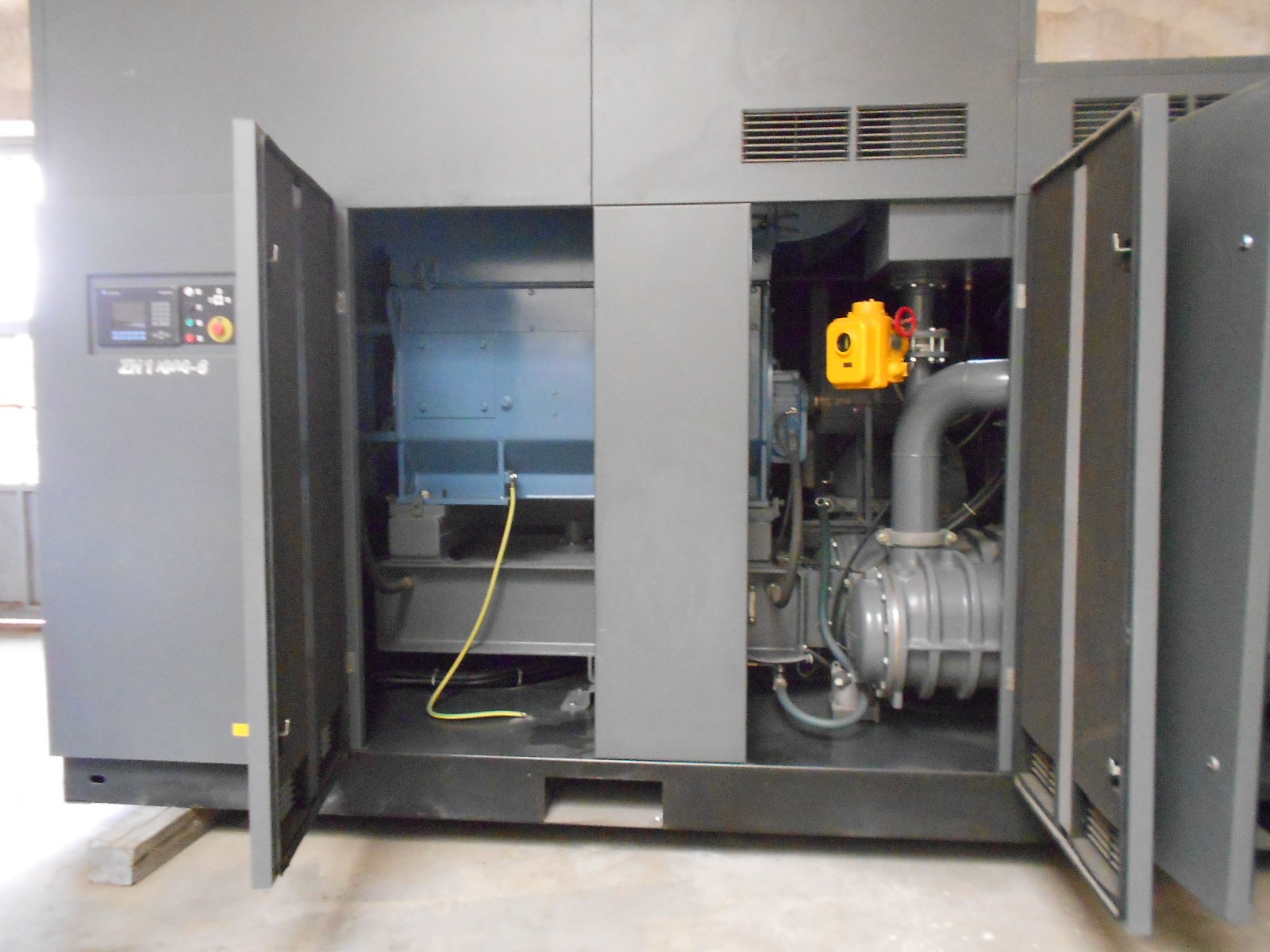 An ATLAS COPCO ZH 10000-6-7PL AIR COMPRESSOR stands indoors on a concrete floor, its front doors open to reveal wiring, pipes, and a control panel on the left side.