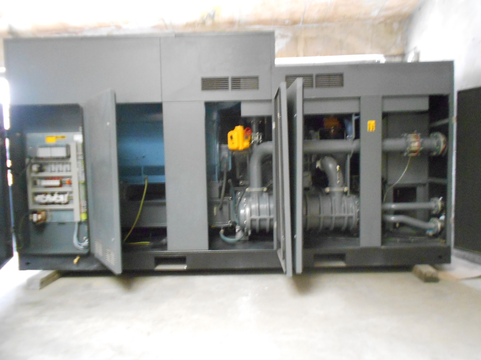 An ATLAS COPCO ZH 10000-6-7PL AIR COMPRESSOR with open panels exposing wiring, pipes, and internal machinery is positioned indoors on a concrete floor.
