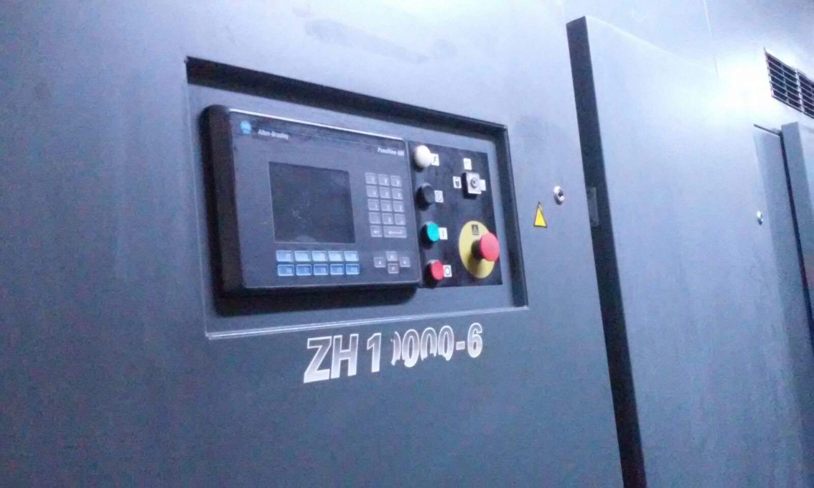 A close-up shows the control panel of an ATLAS COPCO ZH 10000-6-7PL AIR COMPRESSOR, with a display screen, buttons, switches, and emergency stop button mounted on the dark gray machine.