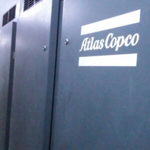An ATLAS COPCO ZH 10000-6-7PL AIR COMPRESSOR with the white logo is installed indoors, likely in a factory or workshop, with other equipment and pipes visible in the background.