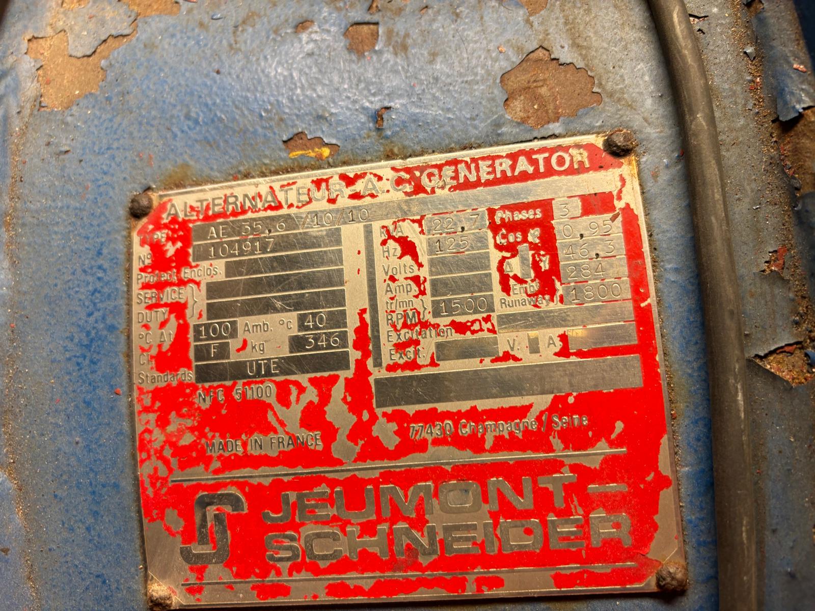 A close-up of a worn and rusted red and silver metal nameplate on a blue machine, labeled ALTERNATEUR M.A. GENERATOR and JEUMONT SCHNEIDER, with faded technical specifications.