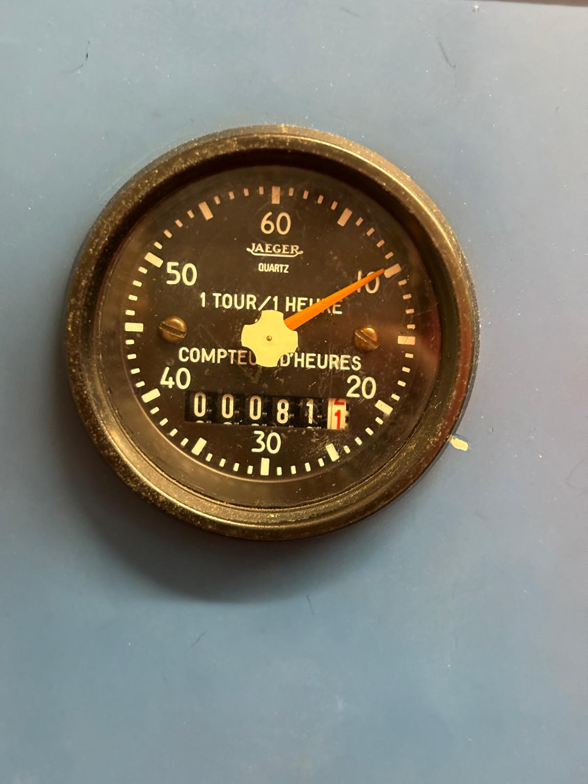 A close-up of a round Jaeger quartz hour meter with a black face, showing 811.7 hours on the display, mounted on a blue surface. The yellow needle points just past 20.