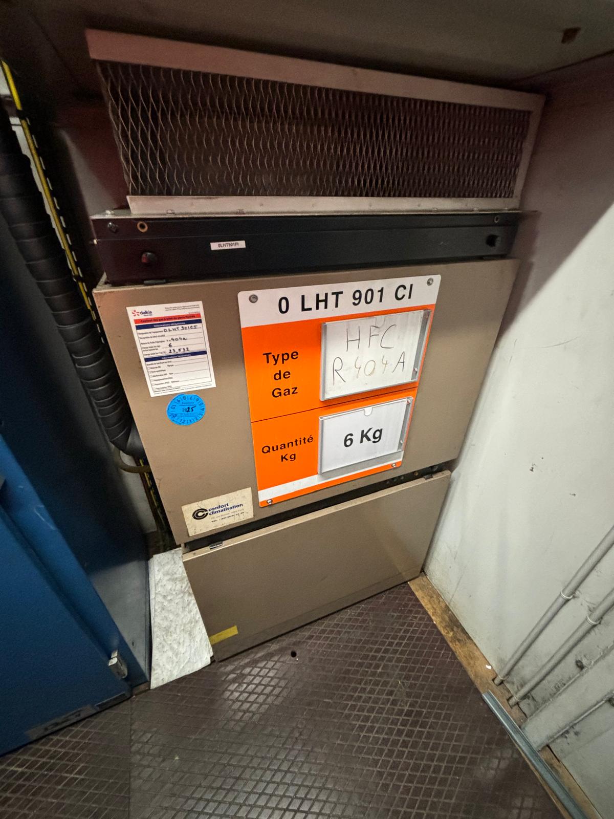 A labeled storage unit with a sign reading 0 LHT 901 CI. The orange label specifies Type de Gaz: HFC R-404A and Quantité: 6 Kg. Industrial equipment and wiring are visible nearby.