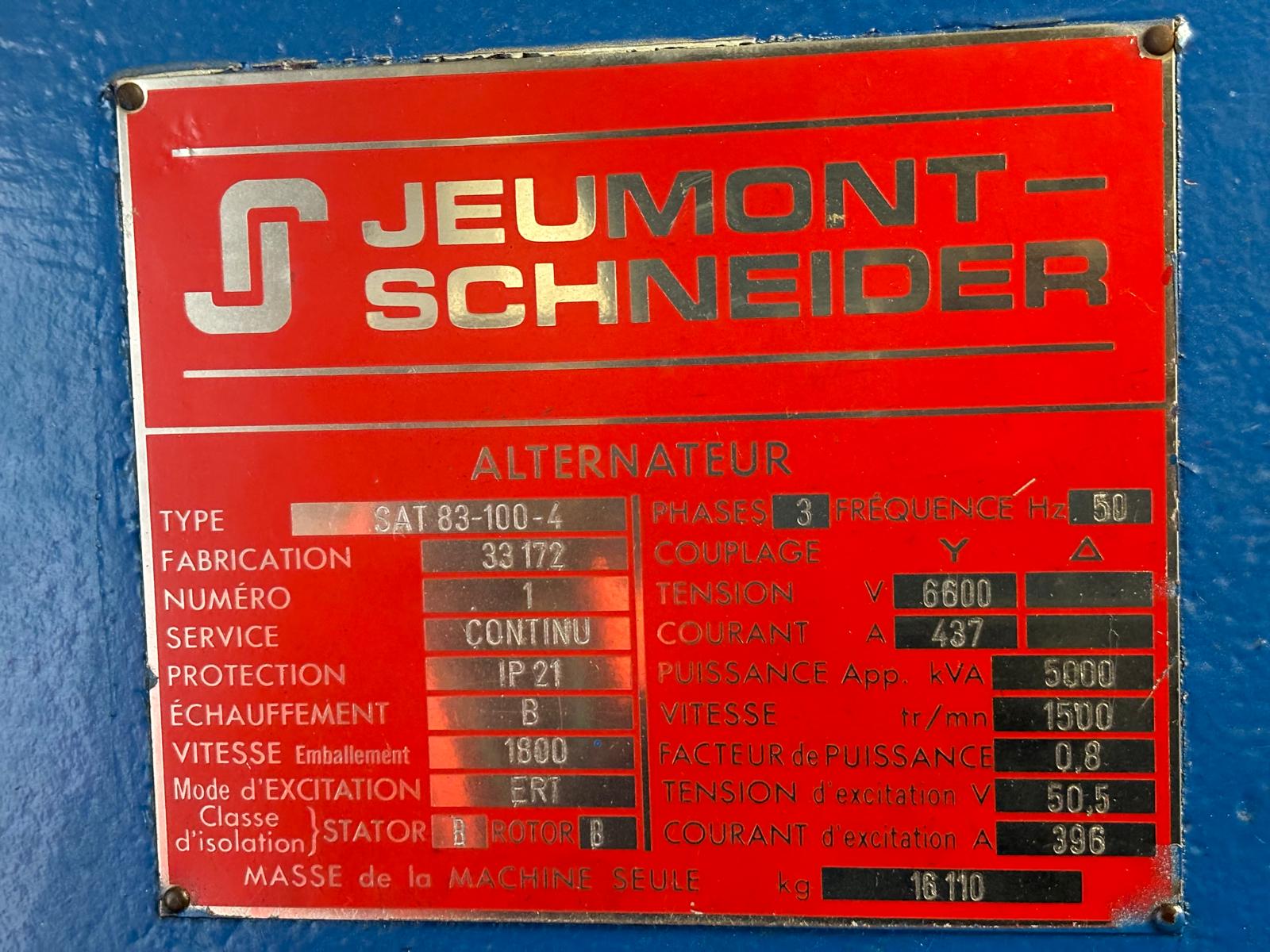 A red and silver metal nameplate on a machine with Jeumont Schneider at the top, displaying technical specifications such as type, voltage, power, frequency, and manufacturing details for an alternator.