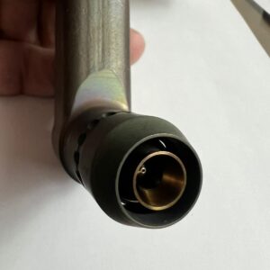 A close-up of a hand holding a metallic device with a cylindrical, brass-colored nozzle at the end, possibly part of a mechanical or plumbing component, set against a white background.