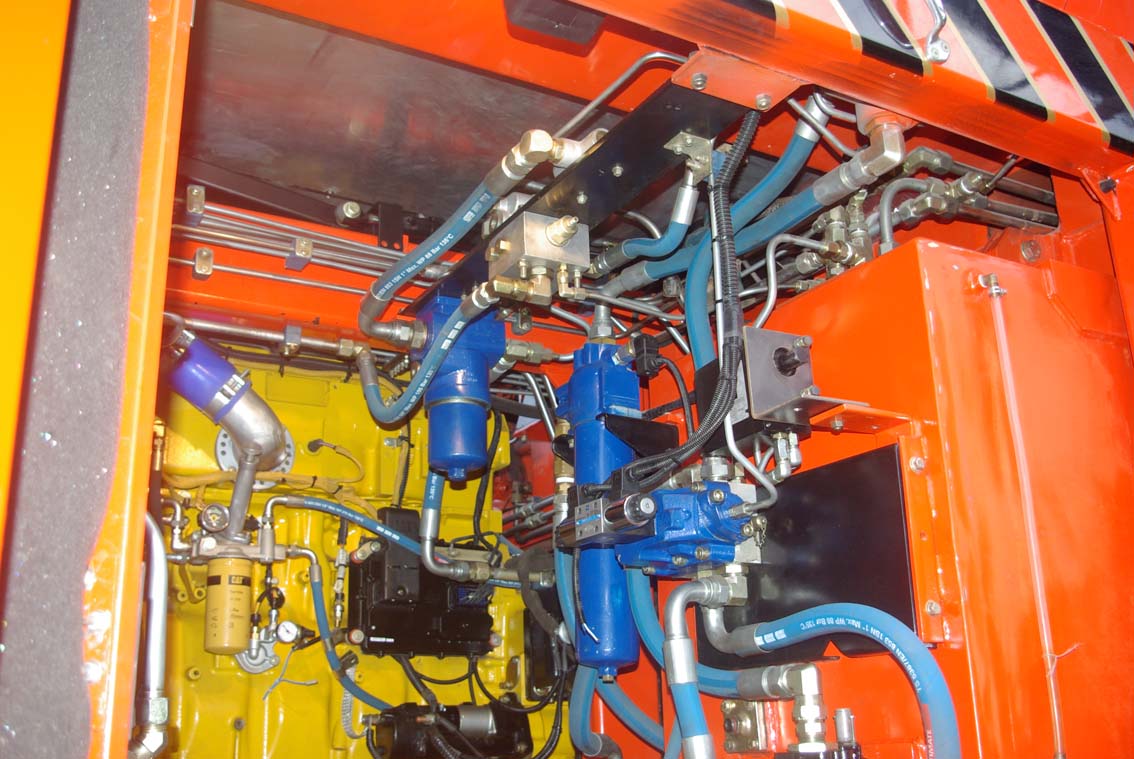 Close-up of AVAILABLE PALING HEAVY TRANSPORTER’s interior, with blue and yellow pipes, hoses, wires, fittings, and metal parts inside an orange and yellow metal enclosure.