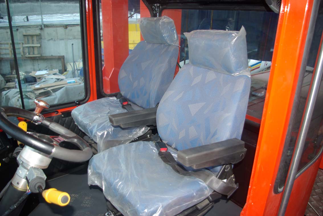 The AVAILABLE PALING HEAVY TRANSPORTER features two blue-patterned seats in clear plastic. The steering wheel and controls are on the left, with large windows showing an industrial Iron Mill setting outside.