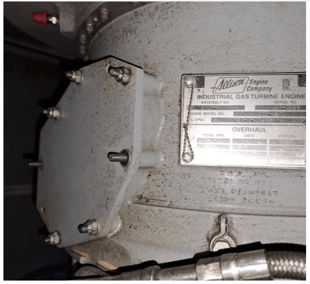 Close-up of a metal machine part with a label reading Allison Engine Company Industrial Gas Turbine Engine. The surface appears dusty, and bolts and a wiring conduit are visible.