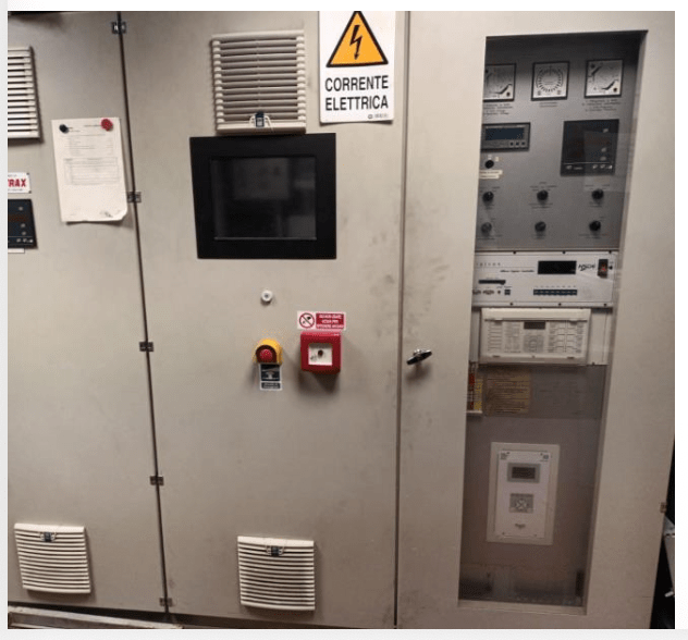Electrical control panel with switches, gauges, a digital screen, warning and emergency buttons, and a “Corrente Elettrica” (Electric Current) caution sign on the door.
