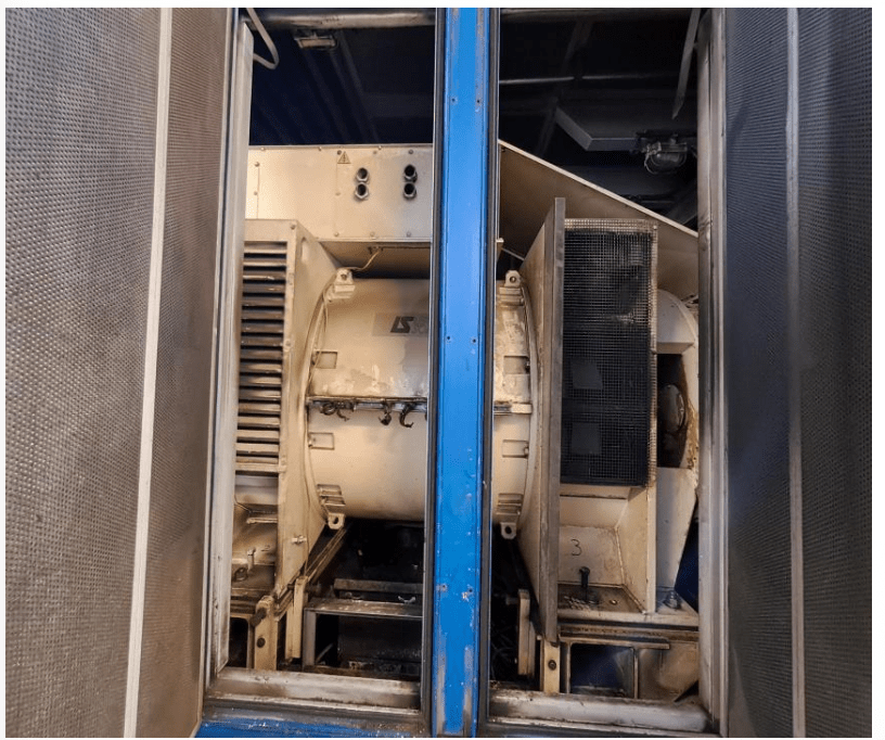 Close-up view of industrial machinery, showing a large, beige motor or generator with ventilation grills and metal framing, enclosed by blue and metallic panels.