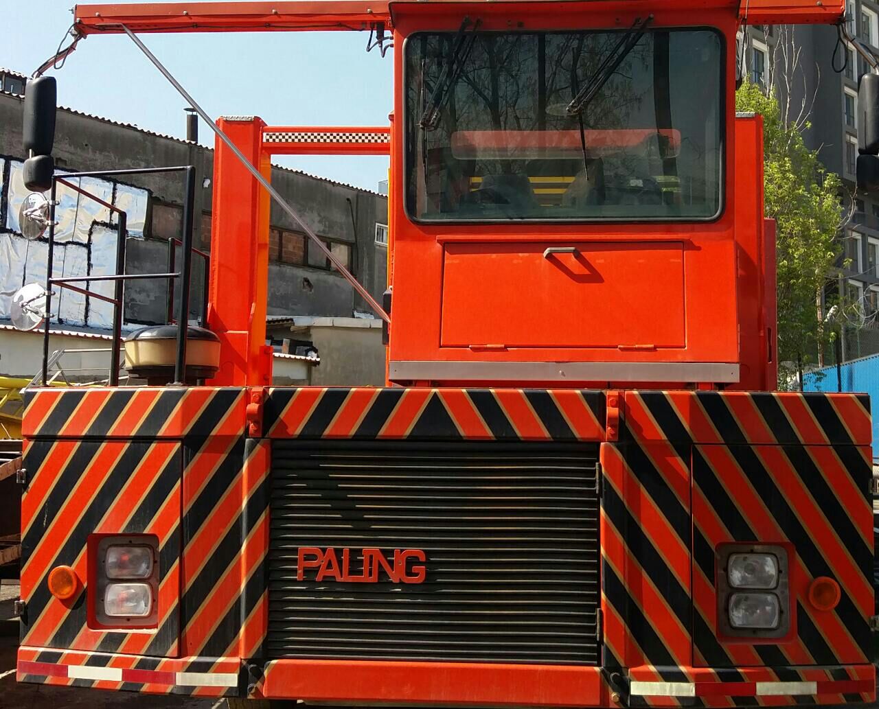 A large red industrial vehicle, likely a crane or heavy-duty truck, with black and yellow diagonal stripes on the front and the word PALING displayed on its grille. Buildings are visible in the background.