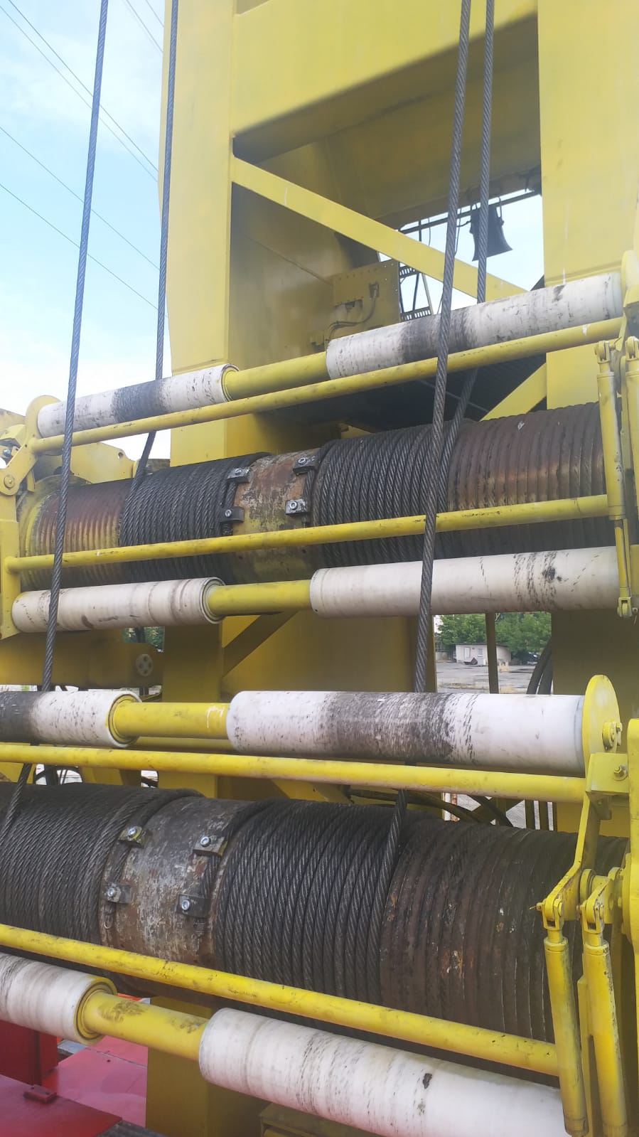 Close-up of thick steel cables wound around dual drums on a yellow AVAILABLE LIEBHERR MOBILE HARBOUR CRANE LHM150, with white cylindrical rollers guiding the cables.