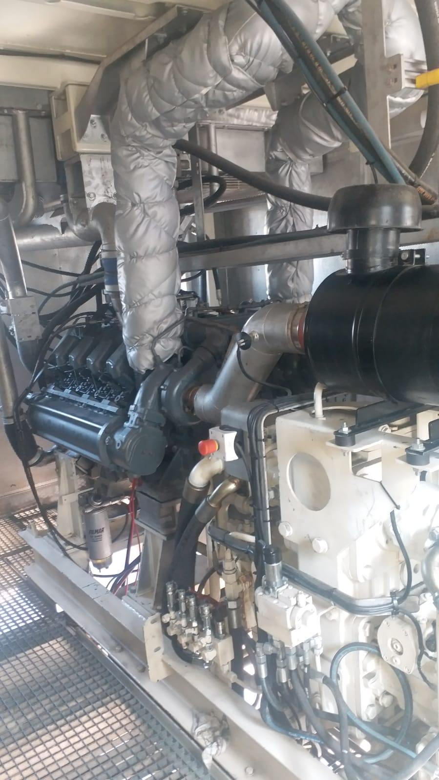 The AVAILABLE LIEBHERR MOBILE HARBOUR CRANE LHM150 features an industrial engine with insulated pipes, wiring, and metallic parts on a grated platform—built for robust operation using complex hoses and fittings in heavy-duty environments.