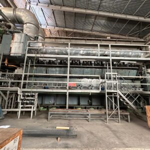 Three used MAN 18V48/60 HFO diesel engines (50 Hz) power plant sets are displayed in a spacious, well-lit factory with metal scaffolding, pipes, and various equipment beneath a corrugated metal roof.