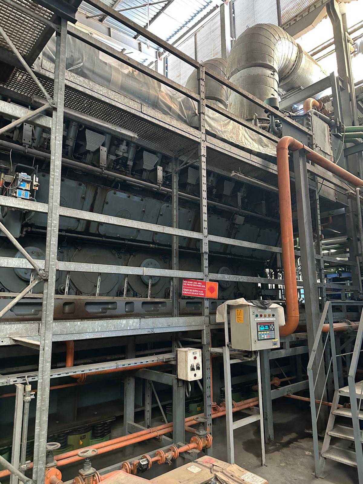 Three sets of used MAN 18V48/60 HFO diesel engines power this 50 Hz plant, shown in an industrial factory with metal platforms, pipes, control panels, ventilation ducts, and visible safety warning signs.