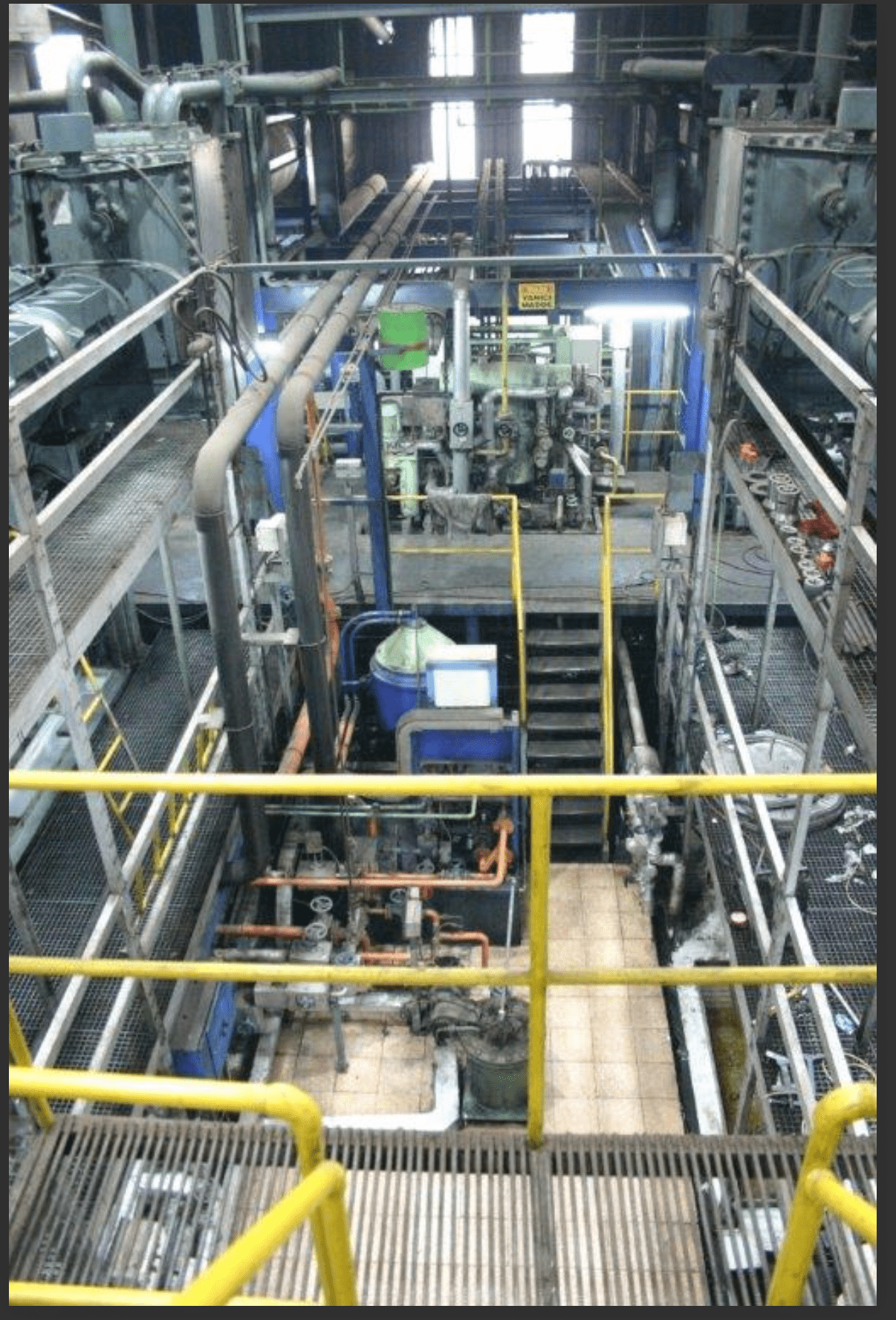 An industrial facility with metal walkways, yellow railings, pipes, and machinery. The brightly lit 3 SETS OF USED 18V48/60 MAN HFO DIESEL ENGINES 50 HZ POWER PLANT features complex equipment and multiple raised work levels.