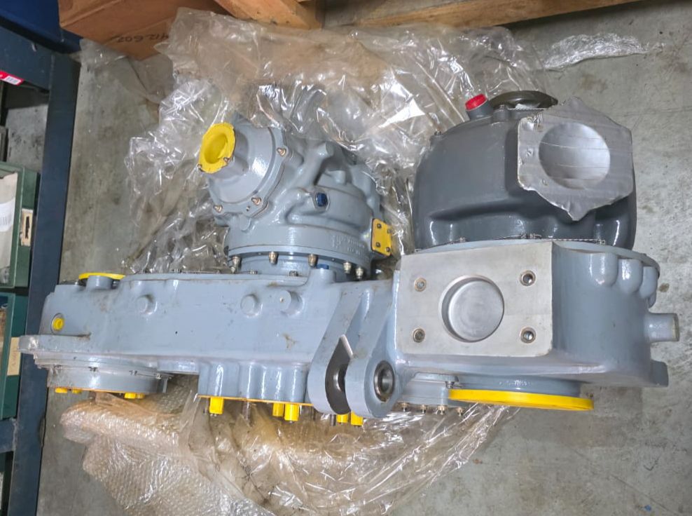 The Gas Turbine Gearbox with Starter and Oil Separator, finished in industrial gray with yellow caps and fittings, is displayed on clear plastic sheeting over a concrete warehouse floor.