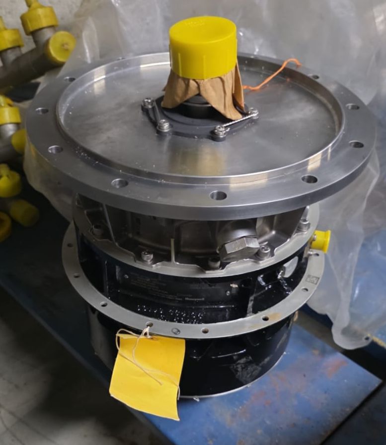 A Gas Turbine Gearbox with Starter and Oil Separator, featuring a round top, yellow protective caps, and a yellow tag, sits on a blue surface with plastic wrapping and other yellow-capped parts in the background.