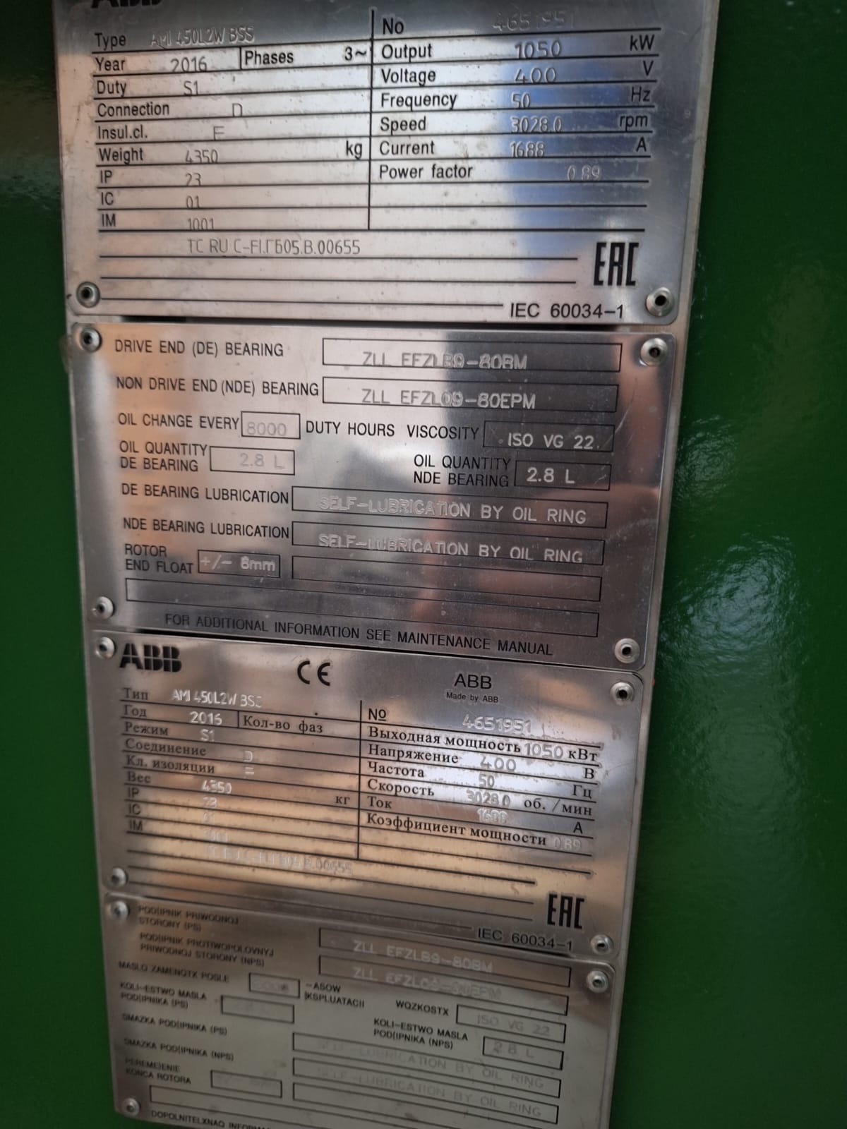 Close-up of metal nameplates with technical information and specifications for ABB machinery, including details on power, voltage, lubrication, bearing type, oil quantity, viscosity, and manufacturer markings. The background is green.