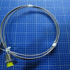 A coiled metal tube with connectors on each end, one covered by a yellow cap, rests on a blue grid-patterned surface—this is the Wanted T3 Temp. Sensor for LM6000 gas turbine, PN L59086P01.